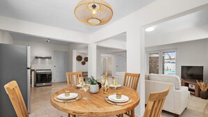 Ein modernes Wohnzimmer mit einem runden Holzes Esstisch, gedeckt für vier Personen, umgeben von Holzstühlen.