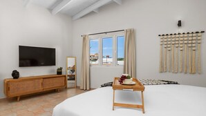 Ein Schlafzimmer mit einem Bett, einem Fernseher, einer Holzkonsole, einem Fenster mit Vorhängen und einer Wandleuchte.