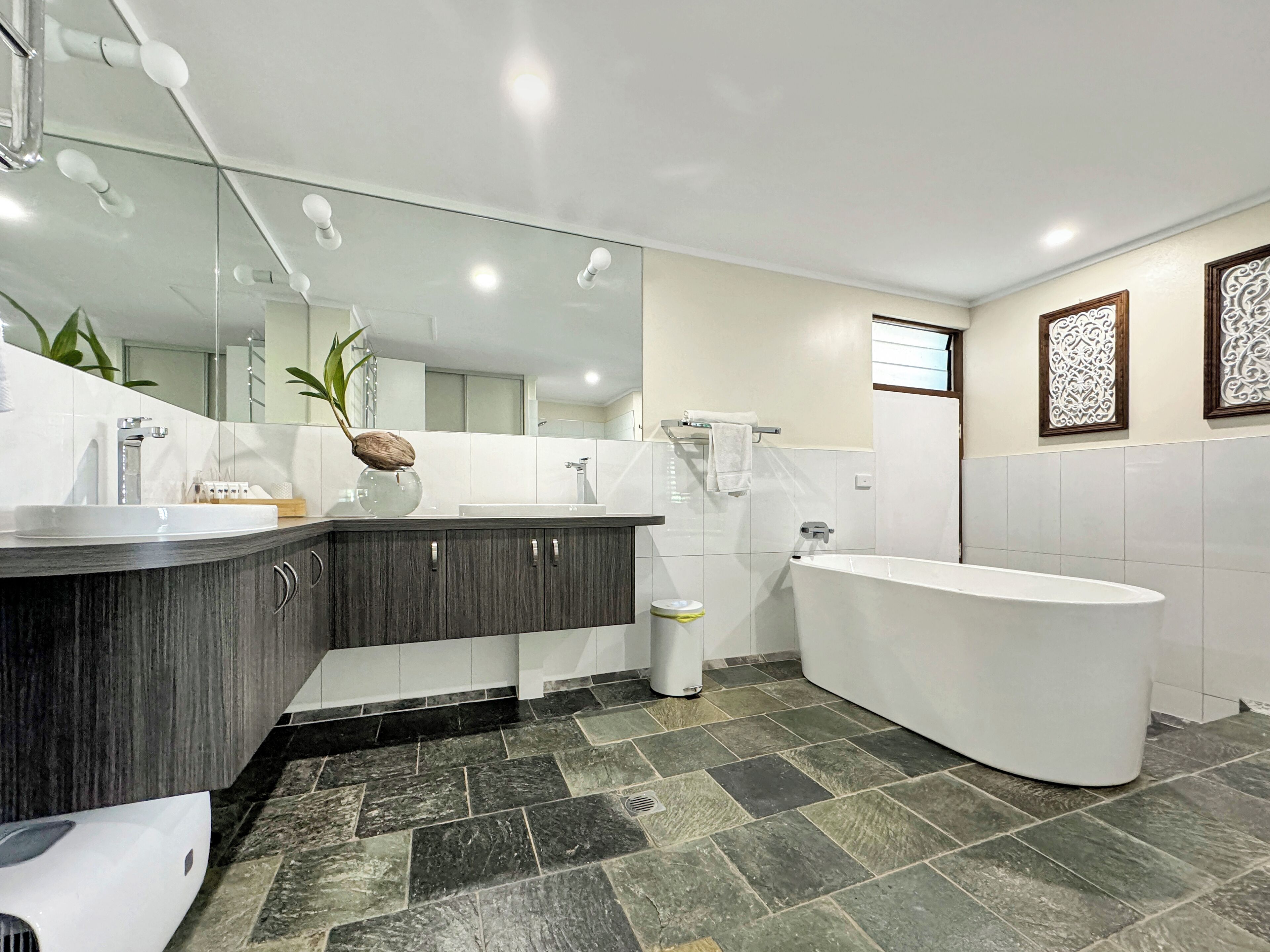 A modern bathroom with a large white bathtub, dark wood vanity, and a large mirror.