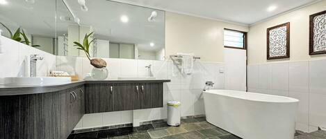 A modern bathroom with a large white bathtub, dark wood vanity, and a large mirror.