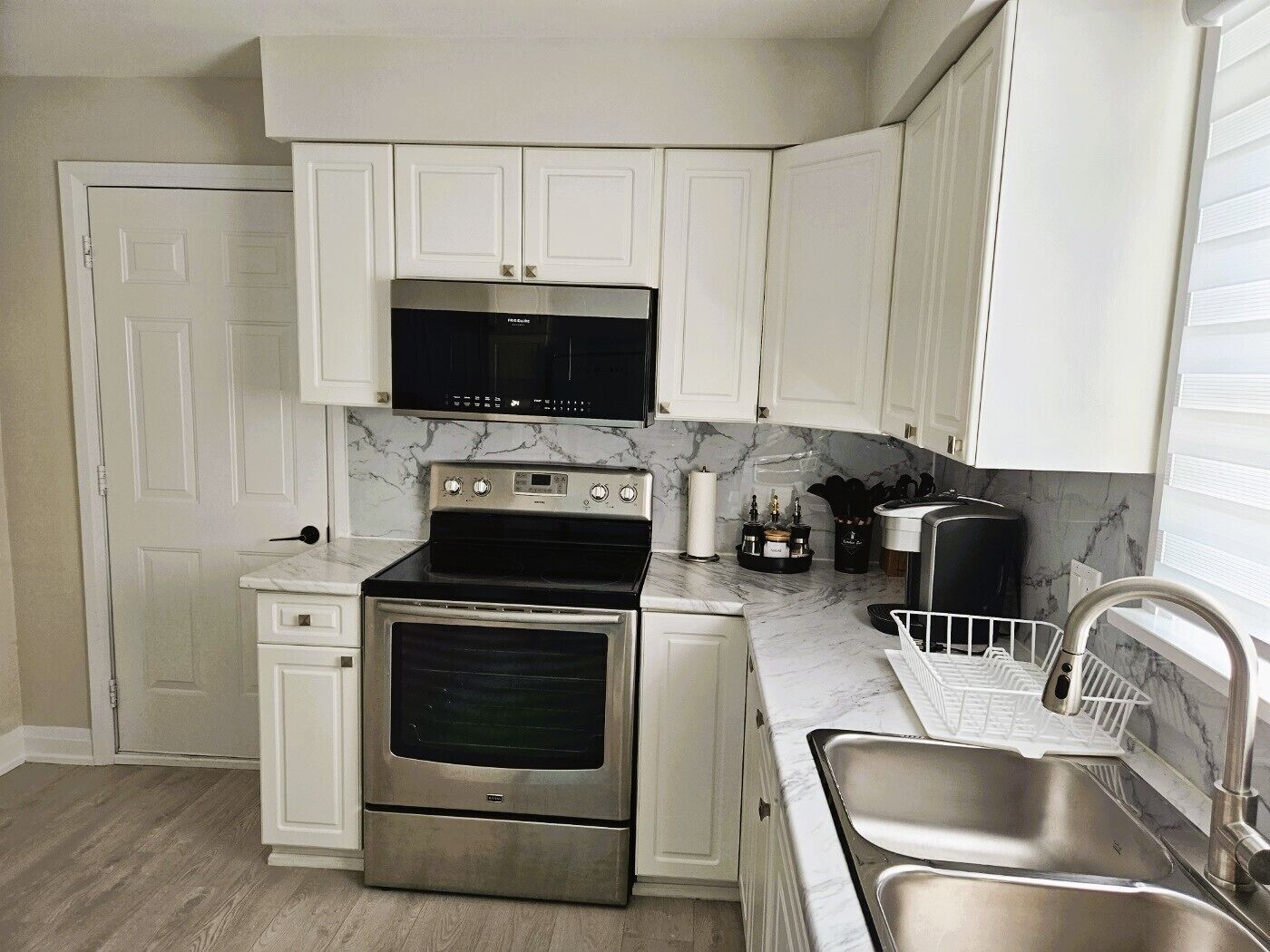A compact kitchen with white cabinets, a stainless steel oven, a microwave, and a sink.