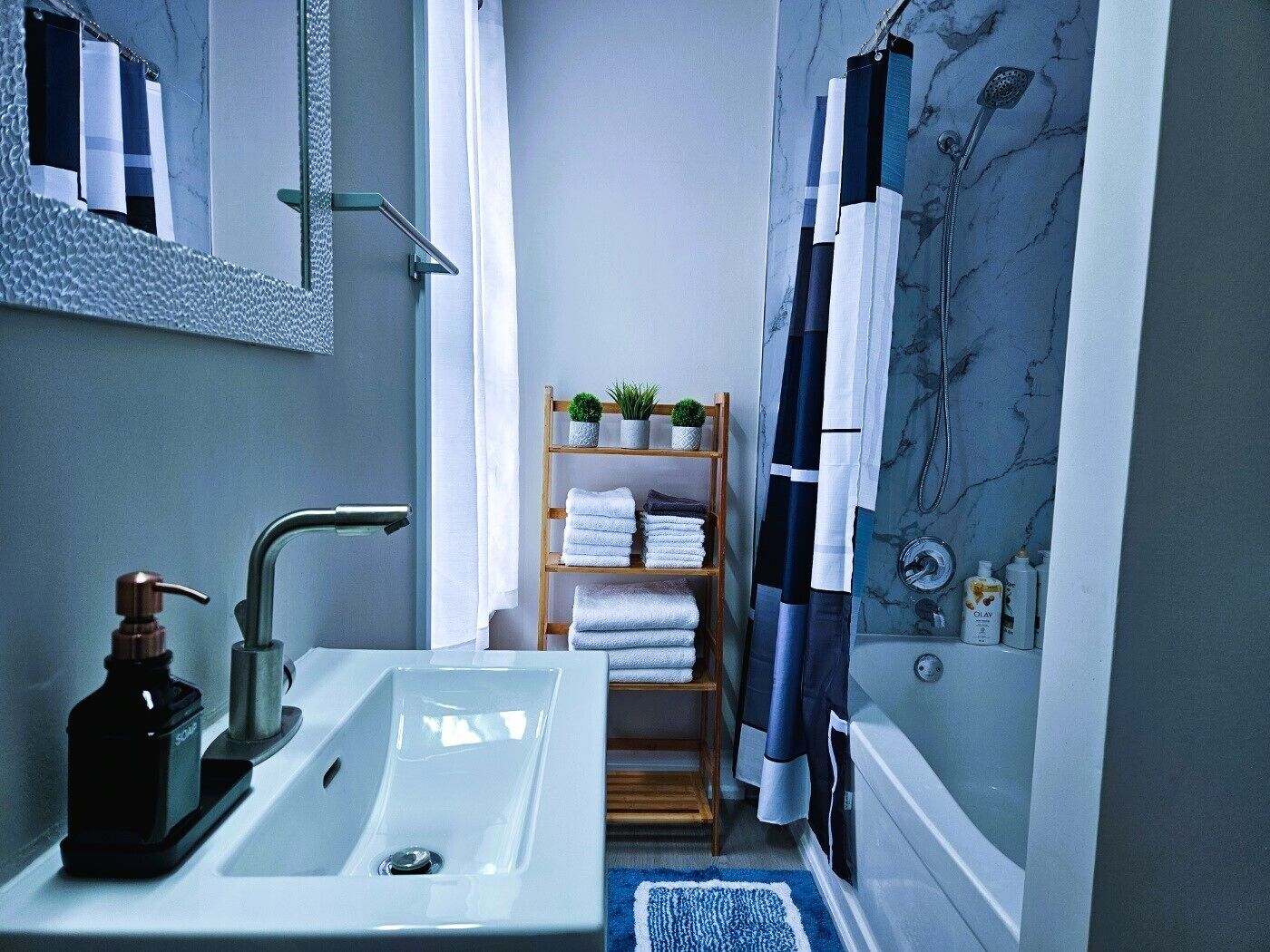 Une salle de bain avec un lavabo blanc, un miroir, une étagère en bois avec des serviettes et un rideau de douche.