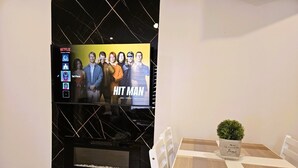 Ett modernt vardagsrum med en platt-TV som är monterad på en svart vägg, ett matbord med en rutig bordslöpare och en krukväxt på bordet.
