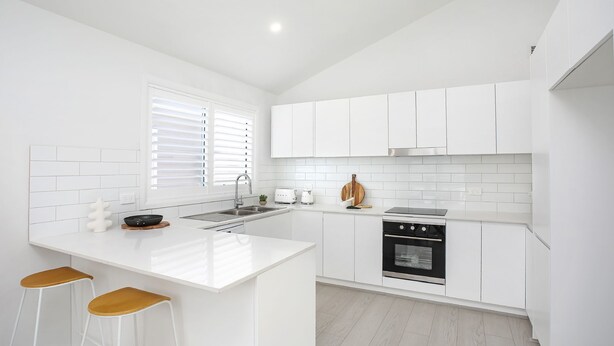 A modern kitchen with white cabinetry, a central island, a built-in oven, and a window with blinds.