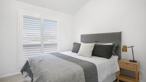 A bedroom with a bed, a bedside table, and a window with blinds.