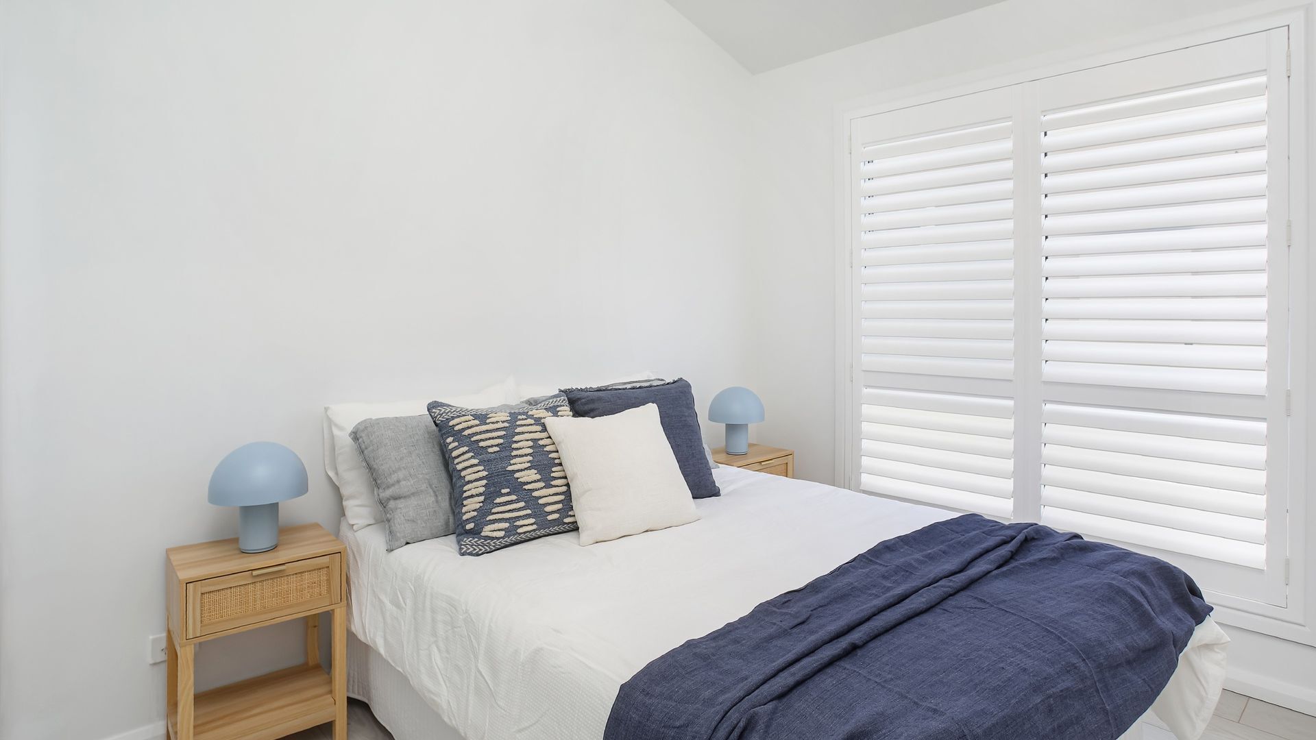 A bedroom with a bed, two bedside tables, and a window with blinds.
