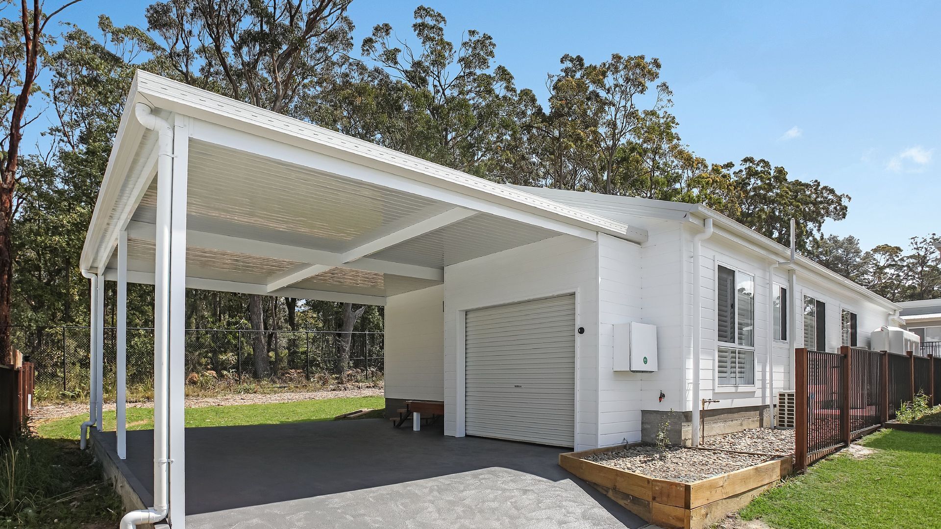 Un'area esterna coperta con un garage, immersa tra alberi e circondata da un giardino recintato.