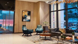 Un hall d'entrée moderne avec des poutres en bois au plafond, un grand lustre, un espace salon avec des canapés et des fauteuils, une table basse et une grande fenêtre donnant sur l'extérieur.
