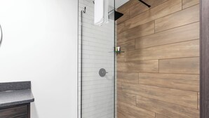 A modern bathroom with a glass shower enclosure, wooden wall paneling, and a marble countertop. - Riverside Retreat | Fishing | WiFi | Pet-Friendly (Aitkin)