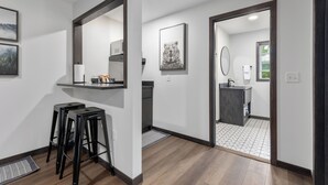 A modern bathroom with a large mirror, a sink, and a toilet. There are two black stools in the adjacent area. - Riverside Retreat | Fishing | WiFi | Pet-Friendly (Aitkin)