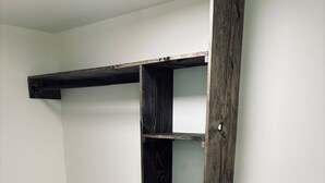 Una habitación con una estantería de madera en la pared, suelo de madera gris y una alfombra azul en el suelo.