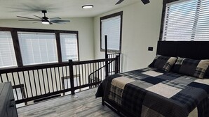 Un dormitorio con cama, ventilador de techo y balcón con barandilla.