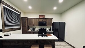 Una cocina con armarios de madera, un refrigerador negro, una encimera blanca y un taburete de madera.