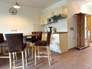 Une cuisine moderne avec un coin repas, comprenant une table et des chaises en bois, une horloge et un four encastré.