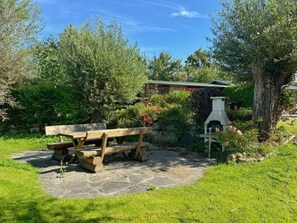 Une terrasse en pierre avec un banc en bois, entourée d’une vég étation luxuriante et d’un mur de pierres.