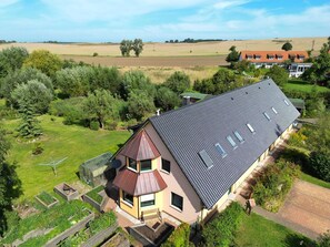 Une maison avec un toit en pente, une petite structure ressemblant à une tour et un jardin avec des plates-bandes surélevées.