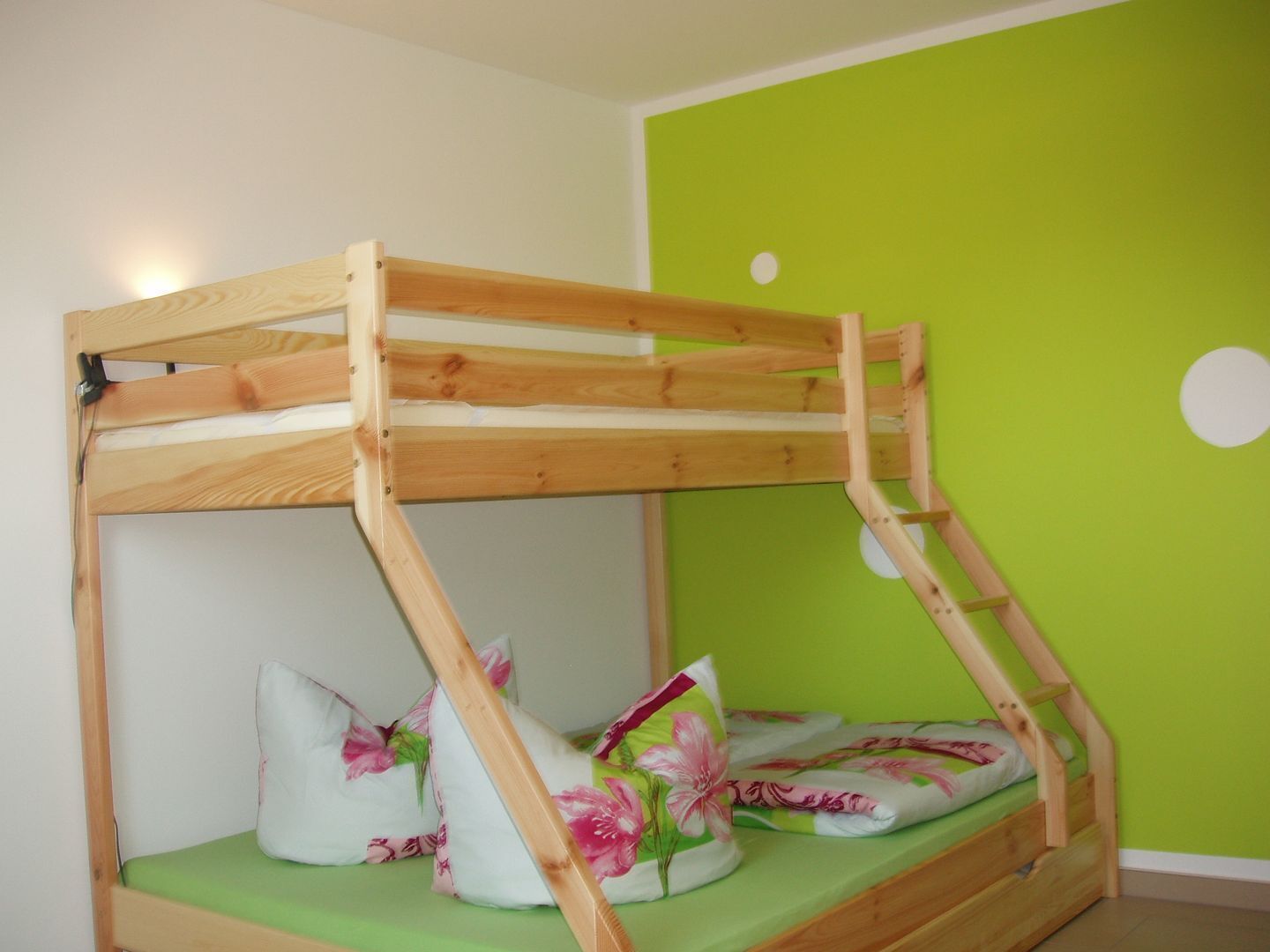 Ein Etagenbett mit Holzrahmen und grüner Matratze, Kissen mit floralen Mustern und eine grüne Wand mit einer weißen, runden Dekoration.