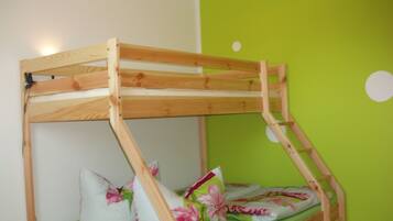 Ein Etagenbett mit Holzrahmen und grüner Matratze, Kissen mit floralen Mustern und eine grüne Wand mit einer weißen, runden Dekoration.