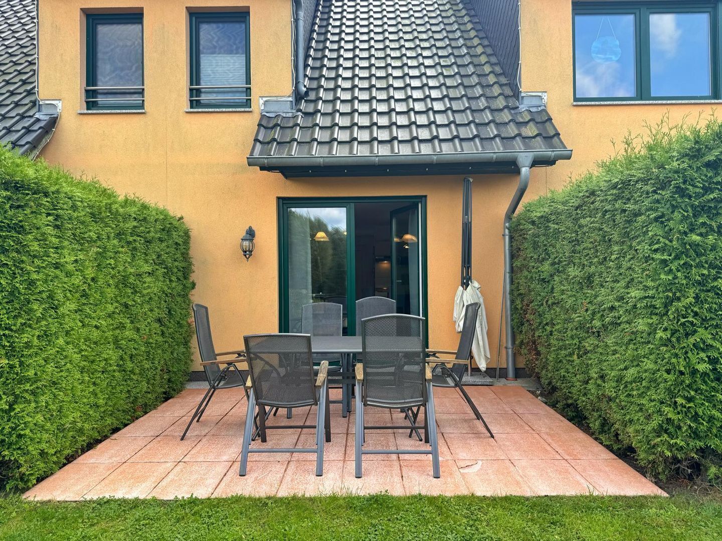 A patio with a table and chairs, surrounded by hedges.