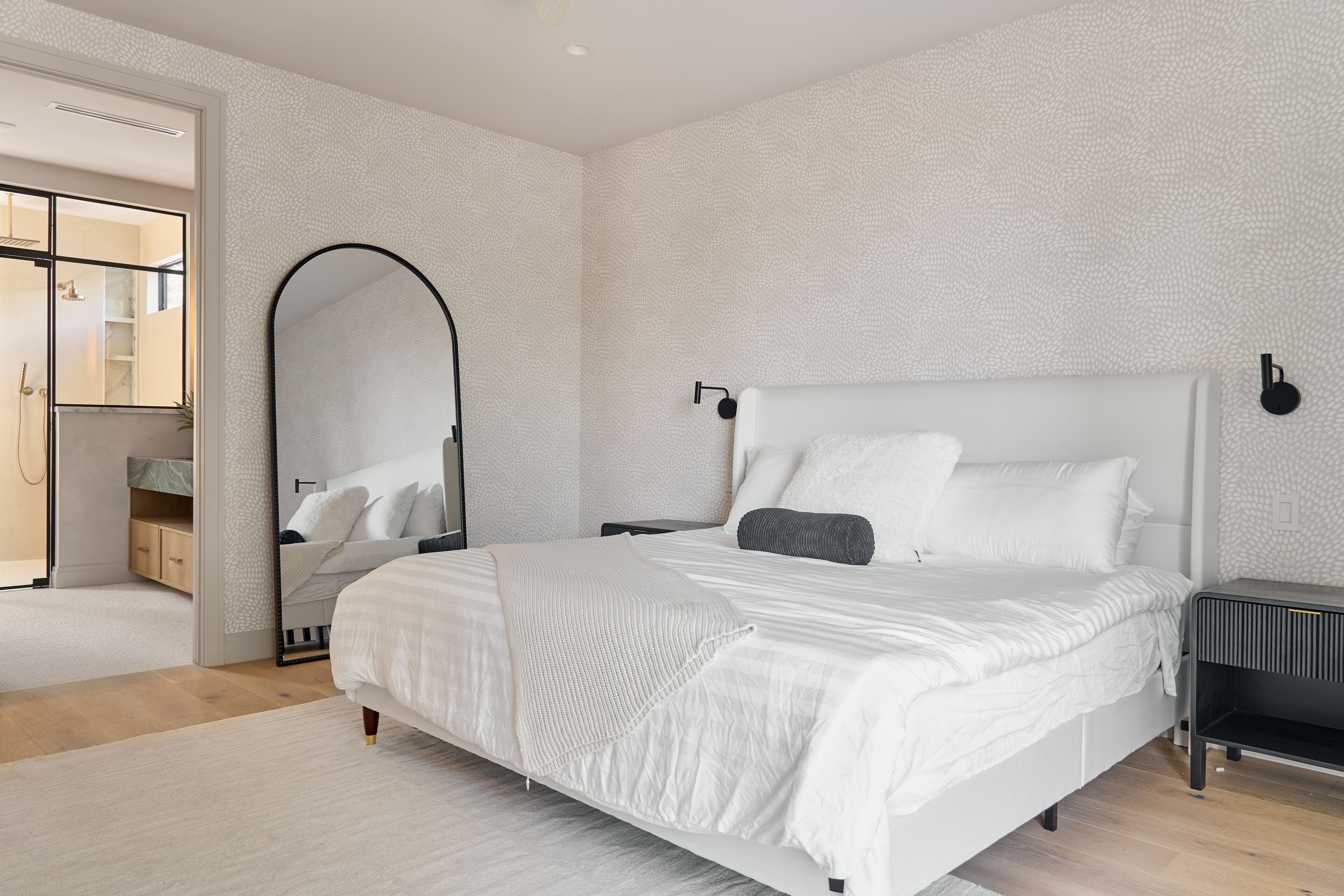 Quarto moderno com uma cama grande, uma mesa de cabeceira, um espelho e um guarda-roupa.
