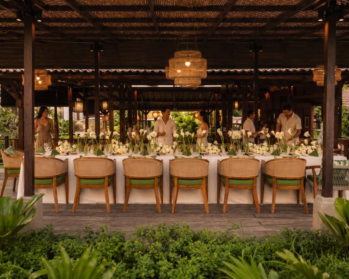 An outdoor dining area with wicker chairs and tables, surrounded by greenery.