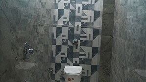 Un bagno con un water bianco, un secchio blu e uno spazio doccia con pareti piastrellate.