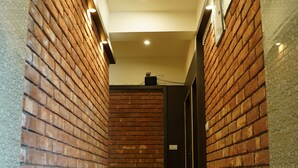 Un corridoio con pareti in mattoni e pavimento in legno, che conduce a una porta in fondo.