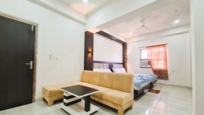 Una camera d'albergo moderna con divano, un tavolino, un letto con testiera, una ventola a soffitto e una finestra con tende.