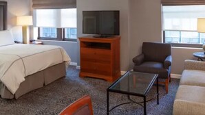 A hotel room with a bed, a television on a wooden stand, a sofa, a chair, and a small table. - The Manhattan Club (New York)