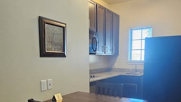 A dining area with a wooden table and chairs, a framed picture on the wall, and a kitchen in the background.