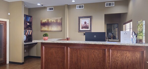 A reception desk with a laptop, framed artwork, and a potted plant. - Dilley Motor Inn (Dilley)