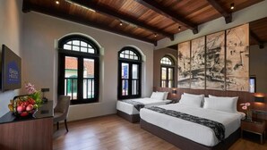 A hotel room with two beds, a desk with a vase of flowers, and a large abstract painting on the wall.