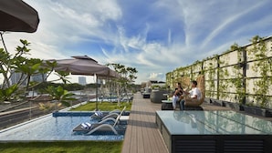A rooftop pool area with lounge chairs, a glass table, and a view of the city skyline.