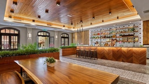 A modern interior with a wooden ceiling, a bar area with shelves, and a seating area with a long wooden table.