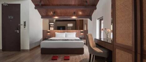 Una habitación de hotel moderna con una cama grande, techo de madera, zona de estar con una silla y un espejo amplio.