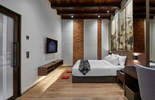 Una habitación de hotel moderna con cama, televisión, banco y una pared decorativa de ladrillo.
