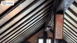 A wooden interior with a sloped ceiling, a balcony railing, and a hanging light fixture.