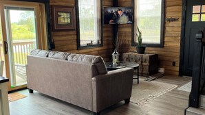 A cozy room with a wooden ceiling, a large window, a television, and a sofa.