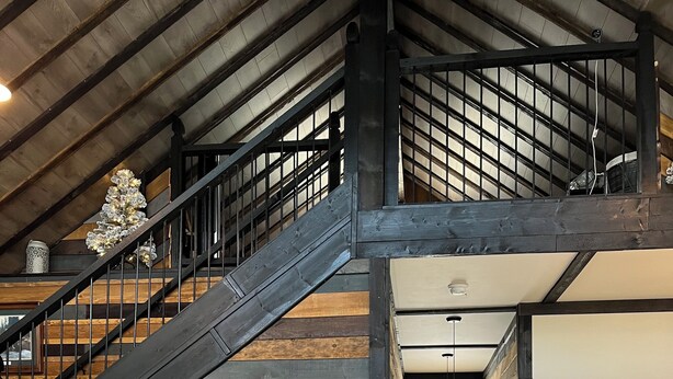 A spacious loft with a wooden staircase, a kitchen with modern appliances, and a view of the outdoors.