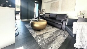 A modern living room with a dark-colored sofa, a round gold coffee table, and a patterned rug. - 1 Bed Barn Retreat - Fireplace, Patio, Parking (Lincoln)