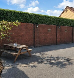 A paved area with a wooden picnic table and a brick wall with a green hedge.