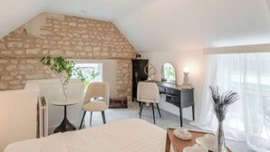 A bedroom with a stone wall, a bed, a desk, two chairs, a small table, and a window with curtains. - 1 Bed Barn Retreat - Fireplace, Patio, Parking (Lincoln)
