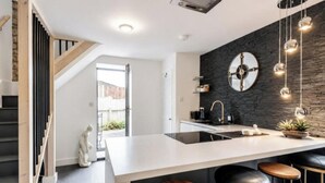 A modern kitchen with a central island, bar stools, and a black backsplash.