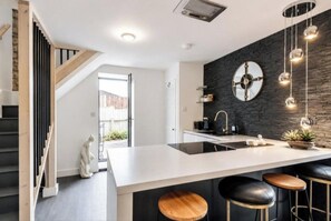 Een moderne keuken met een centraal eiland, barkrukken en een zwarte spatwand.