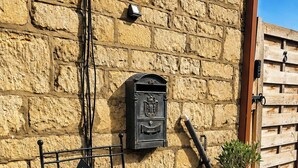 A metal bench with a geometric design, a mailbox, and a potted plant against a textured stone wall.