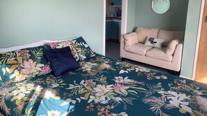 Une chambre à coucher comprenant un lit, un canapé, une horloge murale et une porte donnant sur la cuisine.
