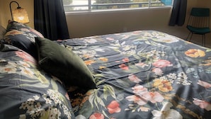 Une chambre à coucher avec un lit, une chaise, une fenêtre donnant sur une rivière et des collines, et une lampe.