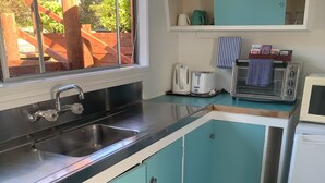 Une cuisine de taille réduite avec des meubles de couleur turquoise, un évier en acier inoxydable, un grille-pain et un four à micro-ondes.