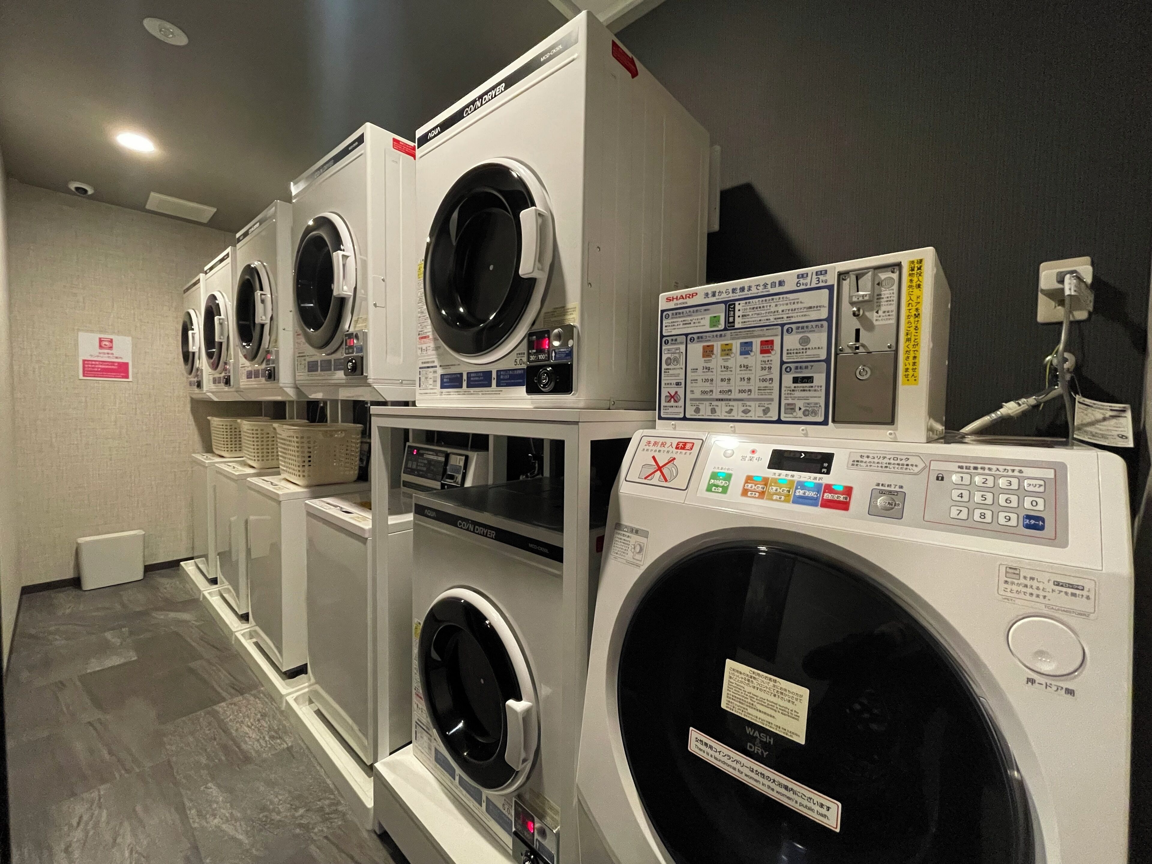 A laundry facility with multiple washing machines and dryers, including a Sharp brand machine.