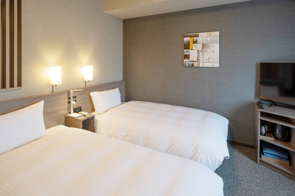 A hotel room with two beds, a TV, a nightstand, and a wall-mounted artwork.